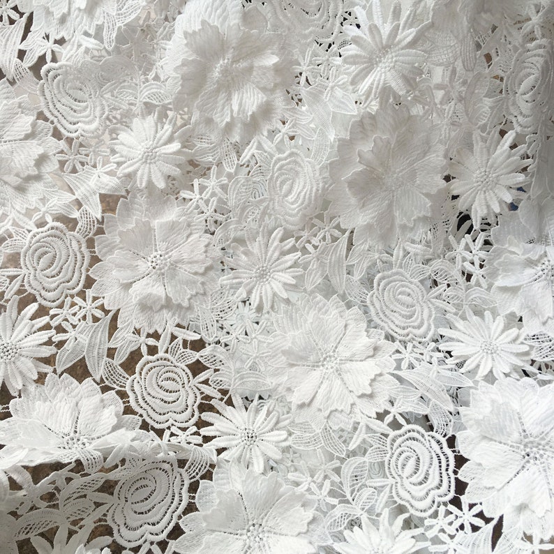Pu&ograve; includere: Tessuto di pizzo bianco con un motivo floreale. Il tessuto &egrave; realizzato in pizzo delicato e intricato con un motivo floreale in rilievo.