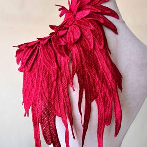 May include: A large, red, feathered applique for clothing or crafts. The applique is made of fabric and has a delicate, layered design.