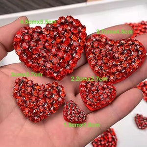 May include: Assortment of red rhinestone heart-shaped embellishments in various sizes. The largest heart measures 4.5 cm by 5.5 cm, while the smallest heart measures 1.5 cm by 1.8 cm.