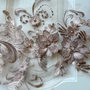 May include: A delicate floral lace applique with a blush pink color. The applique features intricate floral designs with pearl embellishments and rhinestones.