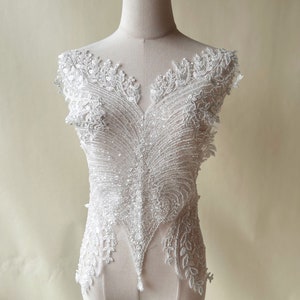 Może przedstawiać: Biała aplikacja z koronek i koralików z dekoltem w kształcie litery V. Aplikacja jest przeznaczona do przyszycia do odzieży.