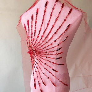 Peut inclure: Embellissement en perles rouges avec un design en éventail. Les perles sont enfilées sur un fil et ont une finition brillante. L'embellissement est parfait pour ajouter une touche d'éclat à n'importe quel vêtement.