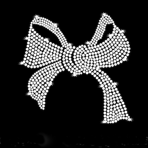 May include: A white rhinestone bow with a large centre loop and two smaller loops on either side. The bow is made of small, round rhinestones that are arranged in a pattern to create the shape of the bow.