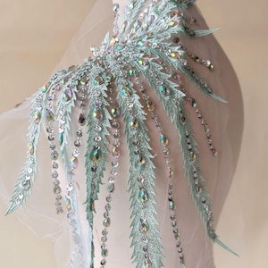 Peut inclure: Une applique de couleur vert clair avec des perles et des paillettes aux accents irisés. L'applique présente un design en cascade avec de longues mèches de perles et de paillettes.