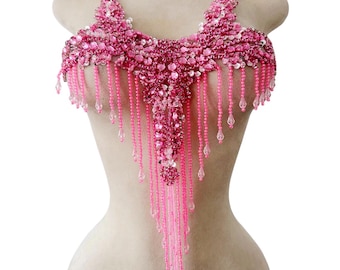 Op de afbeelding: Een roze kralenlijfje met een decoratief ontwerp. Het lijfje heeft een centrale hanger vorm met bungelende kralen strengen. Het ontwerp is versierd met pailletten en kleine, heldere kralen. Het lijfje wordt op een mannequin getoond.