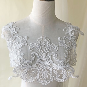 Op de afbeelding: Witte kant applique met een delicaat bloemenmotief. De applique heeft ingewikkelde details en een gegolfde rand.