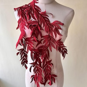 May include: A burgundy embroidered leaf applique. The applique features detailed leaf patterns with a delicate, openwork design. The leaves cascade down, creating a flowing, decorative element. The applique is likely for embellishing garments or crafts.
