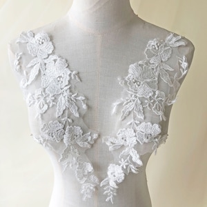 Może przedstawiać: Biała aplikacja koronkowa z kwiatowymi wzorami. Aplikacja zawiera delikatne kwiaty i liście, idealne do dodania odrobiny elegancji do odzieży lub rękodzieła.