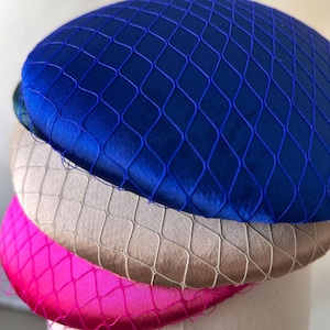 Puede incluir: Primer plano de tres sombreros coloridos. El sombrero superior es azul vibrante, seguido de un sombrero beige y un sombrero rosa brillante. Cada sombrero está cubierto con una red a juego, creando un efecto texturizado. Los sombreros están apilados, mostrando sus diferentes colores y texturas.