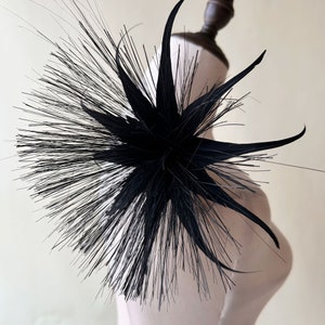 Peut inclure: Une fleur noire en plumes avec de longs pétales pointus. La fleur est attachée à un mannequin blanc.