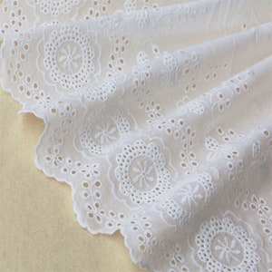 May include: White cotton lace trim with a scalloped edge and a delicate floral pattern. The lace has a subtle sheen and is perfect for adding a touch of elegance to any project.