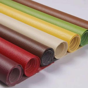 May include: A collection of rolled-up, textured placemats in various colors, including red, brown, yellow, and green. The placemats have a leather-like appearance and are arranged in a diagonal row, showcasing their different hues and textures.