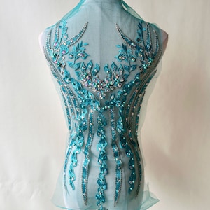 Puede incluir: Aplique de cuentas y lentejuelas de color turquesa con un diseño floral. El aplique está sobre una tela de malla transparente.