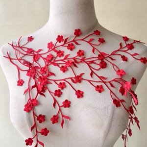 May include: Red floral embroidered applique featuring delicate flowers and leaves on a vine-like design. The applique is displayed on a mannequin, showcasing its potential for embellishing garments or crafts. The vibrant red color adds a touch of elegance.