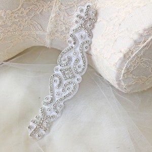 Puede incluir: Una cinta blanca de cuentas con un diseño de diamantes de imitación. La cinta mide aproximadamente 12 pulgadas de largo y tiene un patrón delicado e intrincado.