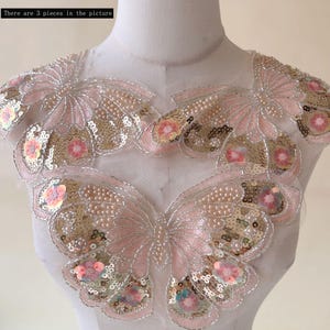 Może przedstawiać: Trzy aplikacje w kształcie motyla. Każda aplikacja ma różowo-złoty wzór z cekinami, z perłowymi koralikami i kwiatowymi akcentami. Aplikacje znajdują się na przezroczystym, białym tle. Widoczny jest tekst "There are 3 pieces in the picture".