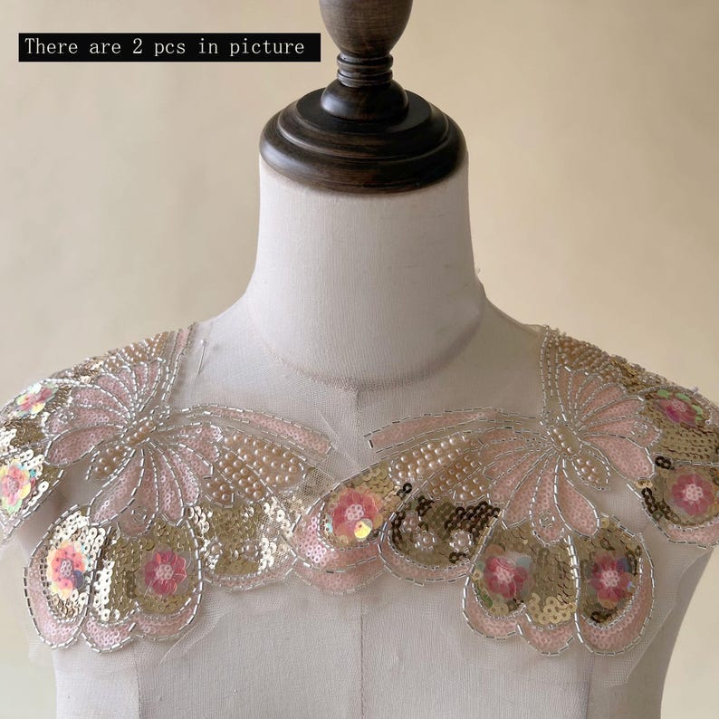 May include: Two decorative shoulder pieces with a floral design. The pieces feature pink, gold, and silver sequins, beads, and embroidery. The text "There are 2 pcs in picture" is visible in the image.
