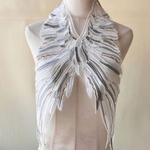 May include: White lace trim with a delicate floral design and gray accents. The trim is shaped like a V-neck and has a scalloped edge.