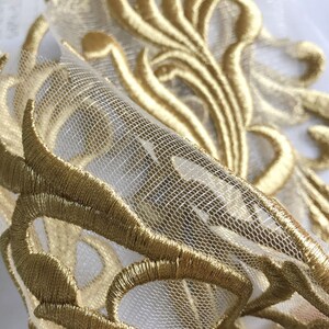 May include: Gold embroidered trim on a sheer white fabric. The embroidery features a delicate floral design.