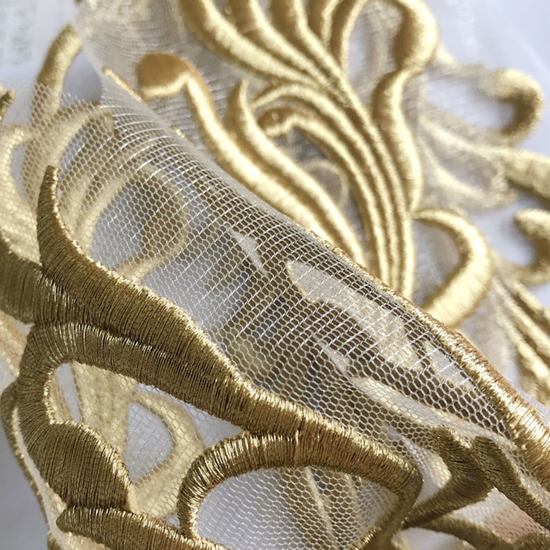 May include: Gold embroidered trim on a sheer white fabric. The embroidery features a delicate floral design.