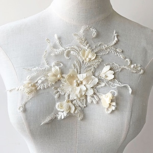 May include: A delicate white floral applique with pearl accents. The applique features a cluster of flowers with intricate lace details. This embellishment is perfect for adding a touch of elegance to clothing, accessories, or home decor projects.