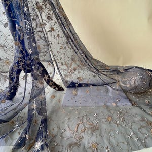 Puede incluir: Tela de tul azul marino bordada con estrellas y lunas doradas y plateadas. La tela es transparente y delicada.