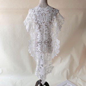 May include: White lace fabric with a delicate floral pattern. The lace is displayed on a white mannequin form.