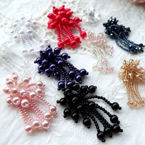 May include: Assortment of pearl and bead embellishments with dangling strands. The embellishments are in various colors, including white, pink, red, purple, black, and gold.