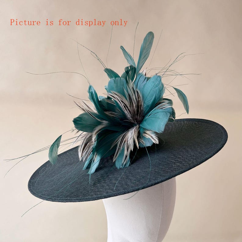 Puede incluir: Un sombrero verde azulado oscuro con ala ancha, adornado con un grupo de plumas verde azulado y grises. El sombrero se exhibe sobre una cabeza de maniqu&iacute; blanca, mostrando su forma y dise&ntilde;o. El texto "Picture is for display only" es visible.