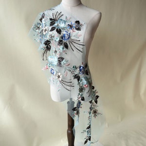 Peut inclure: Un tissu transparent bleu clair avec des motifs floraux brodés noirs, bleus et roses. Le tissu est sur un mannequin.