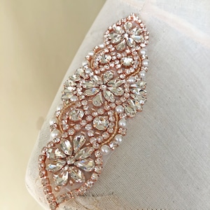 May include: A rose gold embellished trim featuring clear rhinestones and white pearls. The trim is ideal for adding a touch of sparkle to any garment.