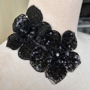Könnte beinhalten: Schwarze Pailletten-Blumenapplikation mit Strassstein in der Mitte. Die Applikation besteht aus schwarzen Pailletten und Netzstoff.