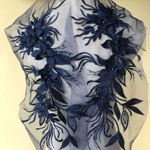 May include: Navy blue floral lace applique with beaded accents. The lace is delicate and intricate, with a variety of flower shapes and sizes. The applique is perfect for adding a touch of elegance to any garment or project.