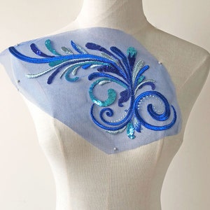 May include: Blue and teal sequined floral applique on a sheer blue fabric. The applique is ideal for adding a touch of sparkle to clothing or crafts.