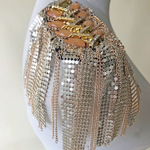 May include: A gold and silver chain shoulder piece with a fringe design. The piece features a cluster of beige and gold embellishments.
