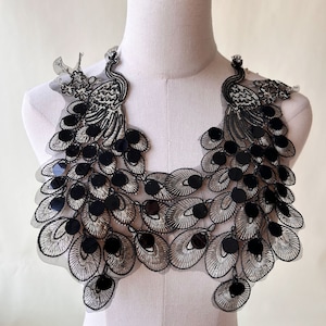 May include: Black and silver peacock-shaped lace applique with sequins. The applique is designed to be sewn onto clothing or other fabric items.
