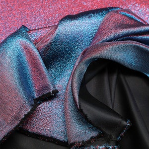 May include: Close-up of a shimmering fabric with a gradient of pink, blue, and black. The fabric has a textured, iridescent finish.
