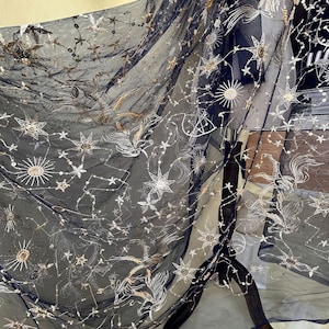 May include: Black sheer fabric with gold and silver embroidered stars and moons. The fabric has a delicate, airy feel.