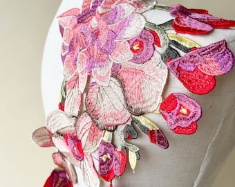 May include: A delicate floral applique featuring pink, red, and purple flowers with green leaves. The applique is perfect for adding a touch of elegance to clothing, accessories, or home decor projects.