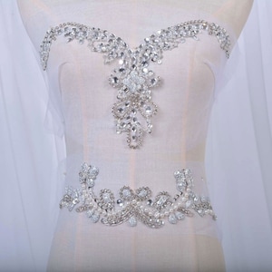 May include: A silver and white beaded embellishment with a floral design. The embellishment is ideal for adding a touch of sparkle to any garment.
