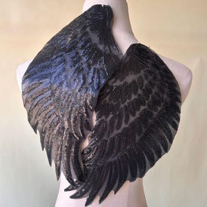 May include: A pair of black sequined angel wings with a sheer mesh backing. The wings are sewn together at the top and are ready to be attached to a garment.