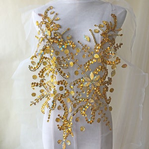 Puede incluir: Aplique de cuentas doradas con un diseño floral. El aplique está hecho de lentejuelas y cuentas iridiscentes, y es perfecto para agregar un toque de brillo a cualquier prenda.