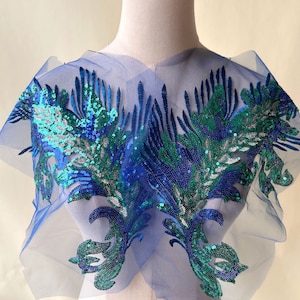 May include: Blue and green sequined applique on a sheer blue mesh fabric. The applique features a floral design with intricate details.