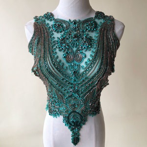 May include: Teal and silver beaded embellishment with a floral design. The embellishment is on a white mannequin.