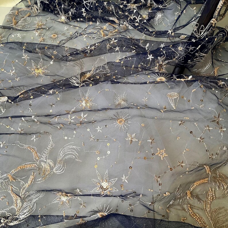 May include: Black tulle fabric with gold embroidered stars and other celestial designs.