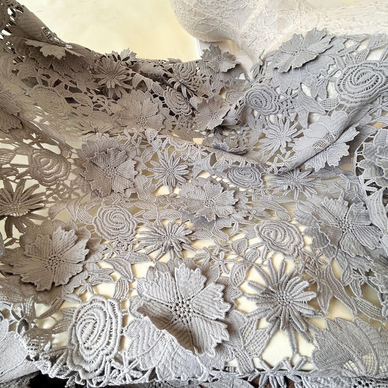 Pu&ograve; includere: Tessuto di pizzo floreale grigio con un design delicato e intricato. Il pizzo presenta una variet&agrave; di forme e dimensioni di fiori, creando un look bellissimo ed elegante.
