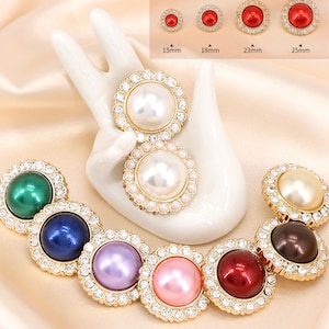 Op de afbeelding: Assortiment van parel- en strassknopen in verschillende kleuren, waaronder groen, blauw, paars, roze en rood. De knopen hebben een diameter van 15 mm, 18 mm, 23 mm en 25 mm.