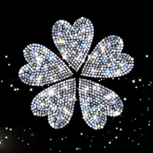 May include: A silver four-leaf clover made of sparkling rhinestones on a black background.