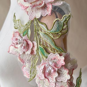 May include: A floral lace appliqué featuring three-dimensional pink and white embroidered flowers with green leaves on a sheer mesh base. The design is accented with white pearl beads and small pink crystals centred within each flower bloom.