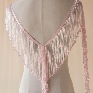 May include: A pink beaded fringe shawl with a V-neck design. The fringe is made of small beads and is very delicate.